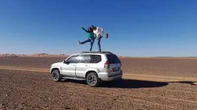 a person standing on the roof of a white car in the desert at Luxury Camp Camelhouse in Merzouga