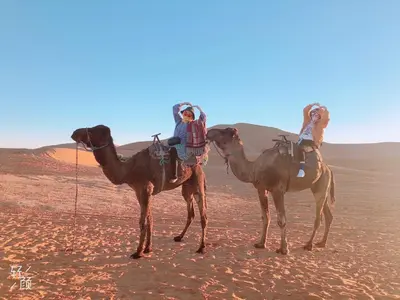 two people riding on the backs of camels in the desert at Luxury Camp Camelhouse in Merzouga
