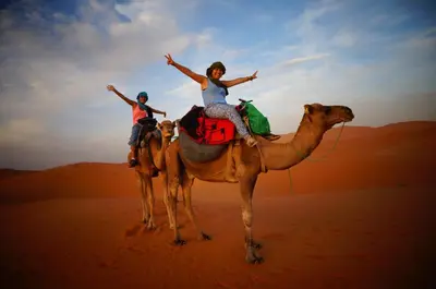 two people riding on the back of a camel in the desert at Luxury Camp Camelhouse in Merzouga