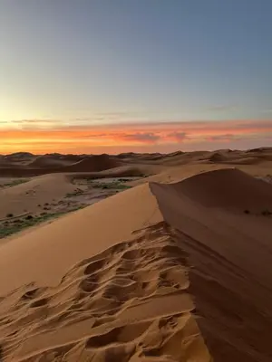 a sunset in the desert with sand dunes at Desert Erg Chegaga Camp in El Gouera