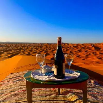 a bottle of wine and two glasses on a table in the desert at Luxury Desert Central Camp in Merzouga