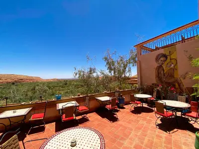 a patio with tables and chairs and a mural at Auberge Ayouze in Aït Ben Haddou