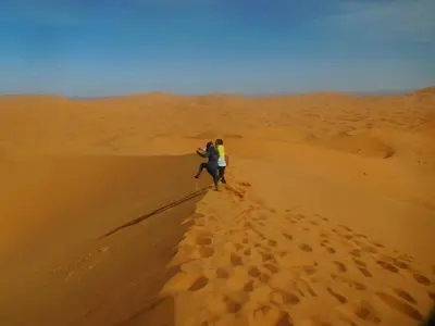 two people walking on a sand dune in the desert at Etoile des Gorges in Aït Baha