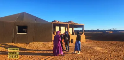 a group of people standing outside of a building in the desert at Kasbah Les Alizes Du Desert in Mhamid