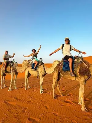 four people riding on the backs of camels in the desert at Sinbad luxury camp in Merzouga