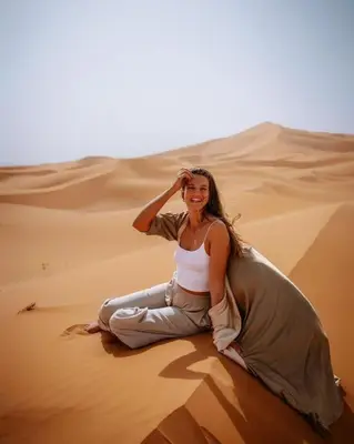 a woman sitting in the sand in the desert at Sinbad luxury camp in Merzouga