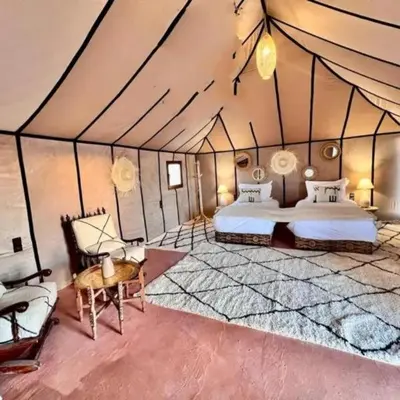 a room with two beds and a table in a tent at Sinbad luxury camp in Merzouga