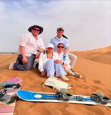 a group of people sitting in the desert with a snowboard at Desert Paradise Luxury Camp in Merzouga
