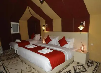two beds with red and white sheets in a room at Desert Paradise Luxury Camp in Merzouga
