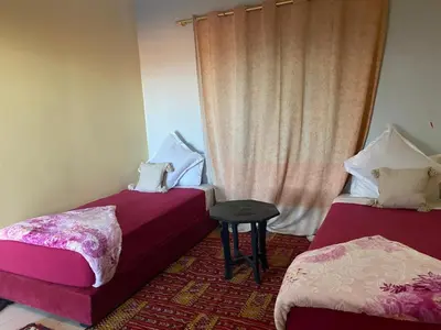 a room with two beds and a stool in front of a window at APPART AIGLE HOTEL in Ouarzazate