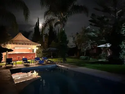 a pool with chairs and a gazebo at night at Villa DALIA - artistic and Cultural Residence in Aghmat