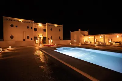 a swimming pool in front of a building at night at Riad Merzouga Dunes in Merzouga