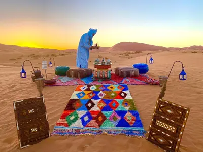 a man standing in the desert with a table in the sand at Jouba Luxury Camp in Merzouga