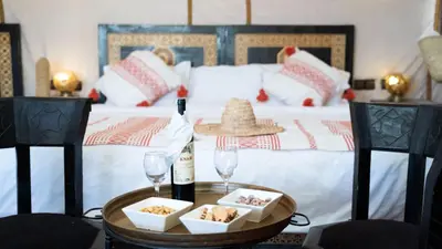 a bed with a table with a bottle of wine and two glasses at Jouba Luxury Camp in Merzouga