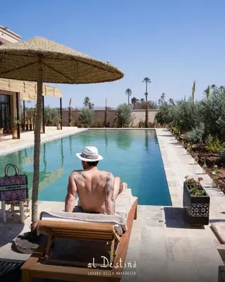 a man sitting in a lounge chair in front of a swimming pool at Al Destino Villa Riad Spa Luxury Marrakech in Marrakech