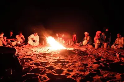 a group of people sitting around a fire on a beach at Chez les habitants in Merzouga