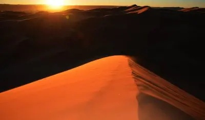 a sunset over a sand dune in the desert at Chez les habitants in Merzouga