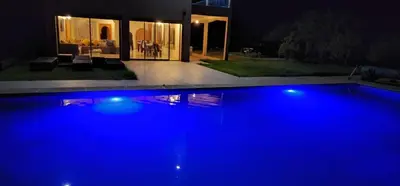 a large blue swimming pool in front of a house at night at Dar HAKIM piscine privée in Marrakech