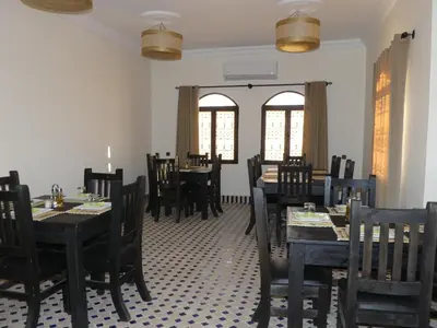 a dining room with tables and chairs and windows at Riad La Luna in Merzouga