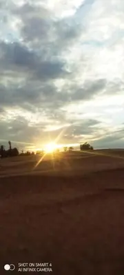 a sunset in the middle of a field with the sun setting at Sahara Camp Light in Mhamid