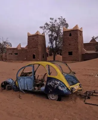 a burnt out car in the middle of a desert at Sahara Camp Light in Mhamid