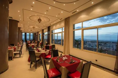 a restaurant with tables and chairs and windows at Hotel Tafilalet in Meknès