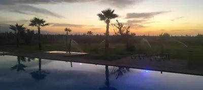 a pool with palm trees and a sunset in the background at Igrane House in Marrakech