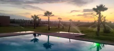 a swimming pool with palm trees and a sunset at Igrane House in Marrakech