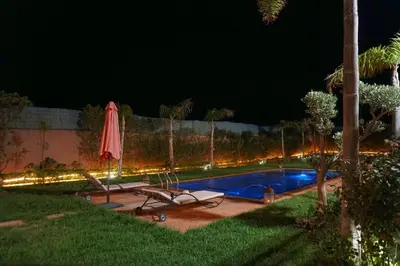 a pool at night with two chairs and an umbrella at Villa Treasure of Marrakech in Marrakech