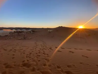 a sunset in the desert with a rainbow in the sand at Merzouga Heart Luxury Camp in Merzouga