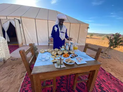 a man standing next to a table in front of a tent at Merzouga Heart Luxury Camp in Merzouga