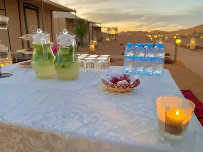 a table with bottles and a candle and a bowl of fruit at Merzouga Heart Luxury Camp in Merzouga