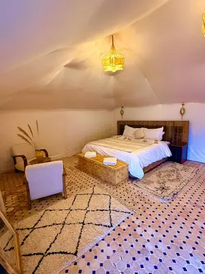 a bedroom with a bed and a table and a chair at Taghit Sahara Camp in Merzouga