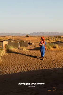 a woman walking down a dirt road in the desert at Tinfou desert camp in Beni Ali