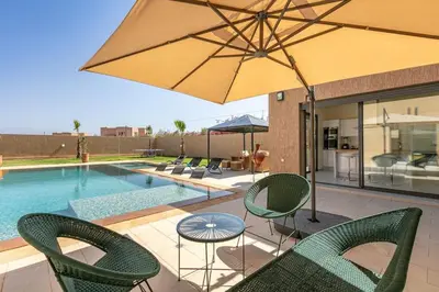 a patio with chairs and an umbrella next to a pool at Villa Sanna, élégante avec piscine Chauffée, jeux in Marrakech