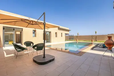 a patio with chairs and an umbrella next to a pool at Villa Sanna, élégante avec piscine Chauffée, jeux in Marrakech