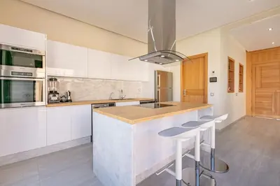 a kitchen with white cabinets and a island with bar stools at Villa Sanna, élégante avec piscine Chauffée, jeux in Marrakech