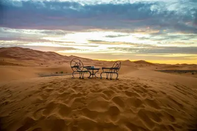 two chairs and a table in the desert at Merzouga Prestige Camp in Merzouga
