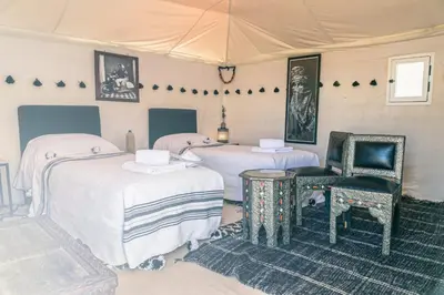 a bedroom with three beds and a chair at Merzouga Prestige Camp in Merzouga