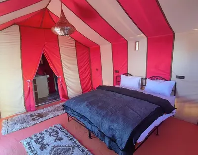 a bedroom with a red and white tent with a bed at Merzouga Magic Carpet camp in Merzouga