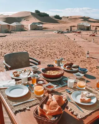 a table with food and bread on the beach at Merzouga Magic Carpet camp in Merzouga