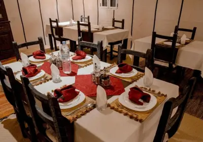 a dining room with white tables and chairs with red food on them at Merzouga Magic Carpet camp in Merzouga