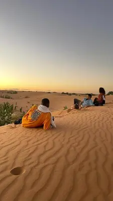 three people sitting on the sand in the desert at Camp Familia Erg Chebbi in Merzouga
