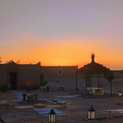 a sunset in the desert with an umbrella and tables at Camp Familia Erg Chebbi in Merzouga