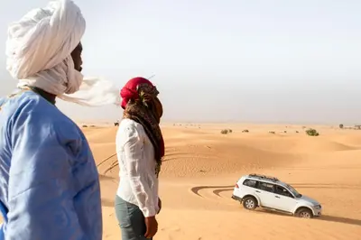 two people standing in the desert looking at a car at Camp Familia Erg Chebbi in Merzouga