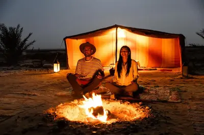two people sitting next to a fire in front of a tent at Camp Familia Erg Chebbi in Merzouga
