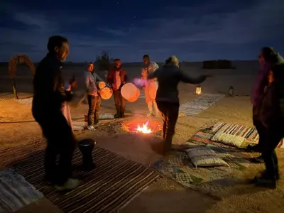 a group of people standing around a fire on the beach at Camp Familia Erg Chebbi in Merzouga