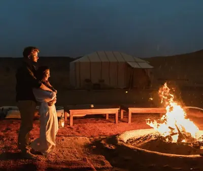 a man and a woman standing next to a fire at Merzouga luxury magic nights in Merzouga