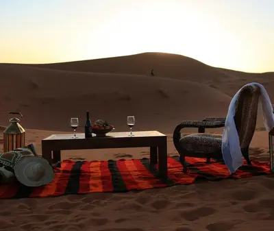 a table and chair in the desert with wine glasses at Merzouga luxury magic nights in Merzouga