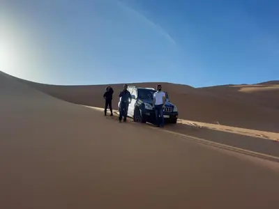 a group of people standing next to a car in the desert at Merzouga Majestic Camp in Merzouga